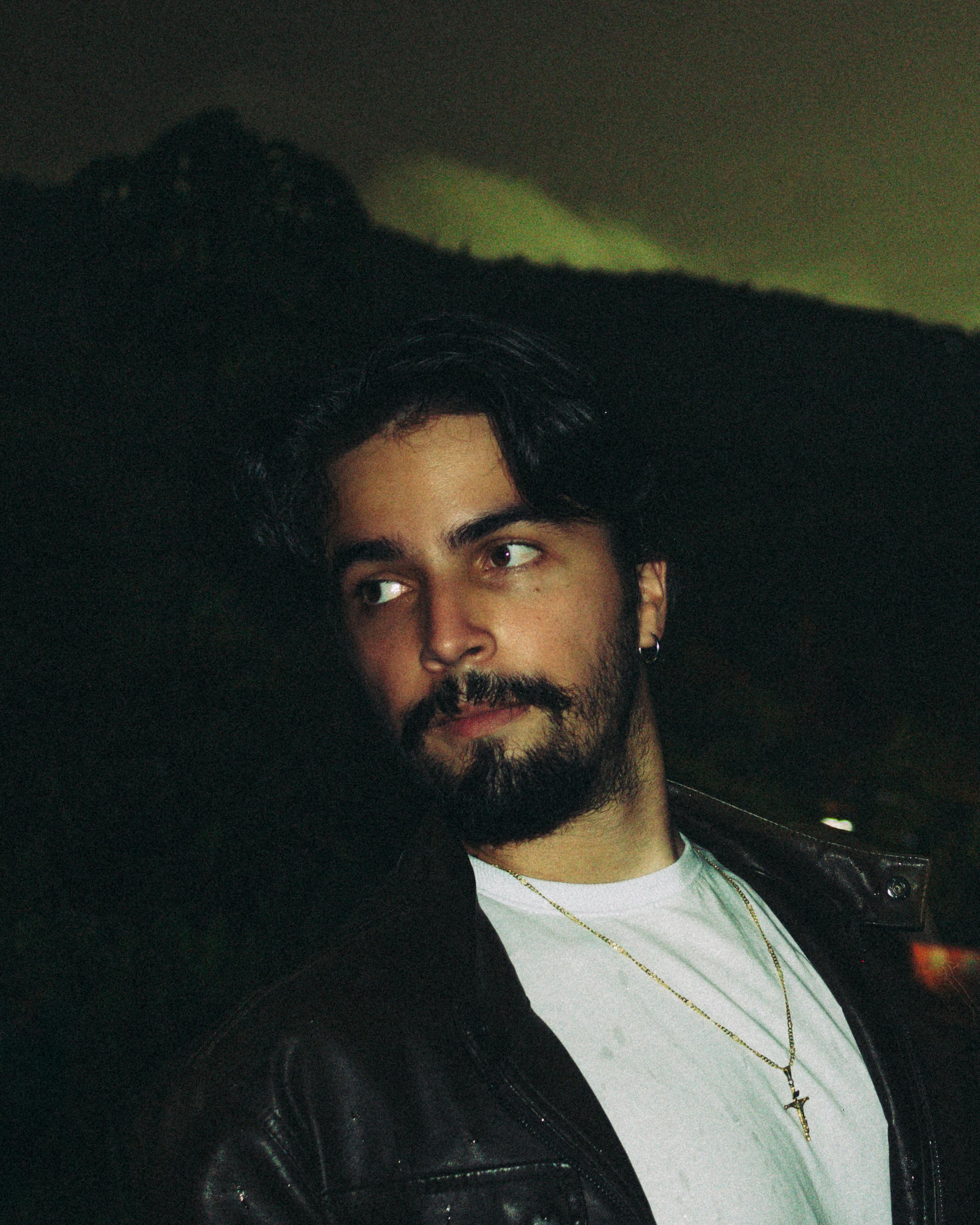 A moody portrait of a young bearded man in a leather jacket at night.
