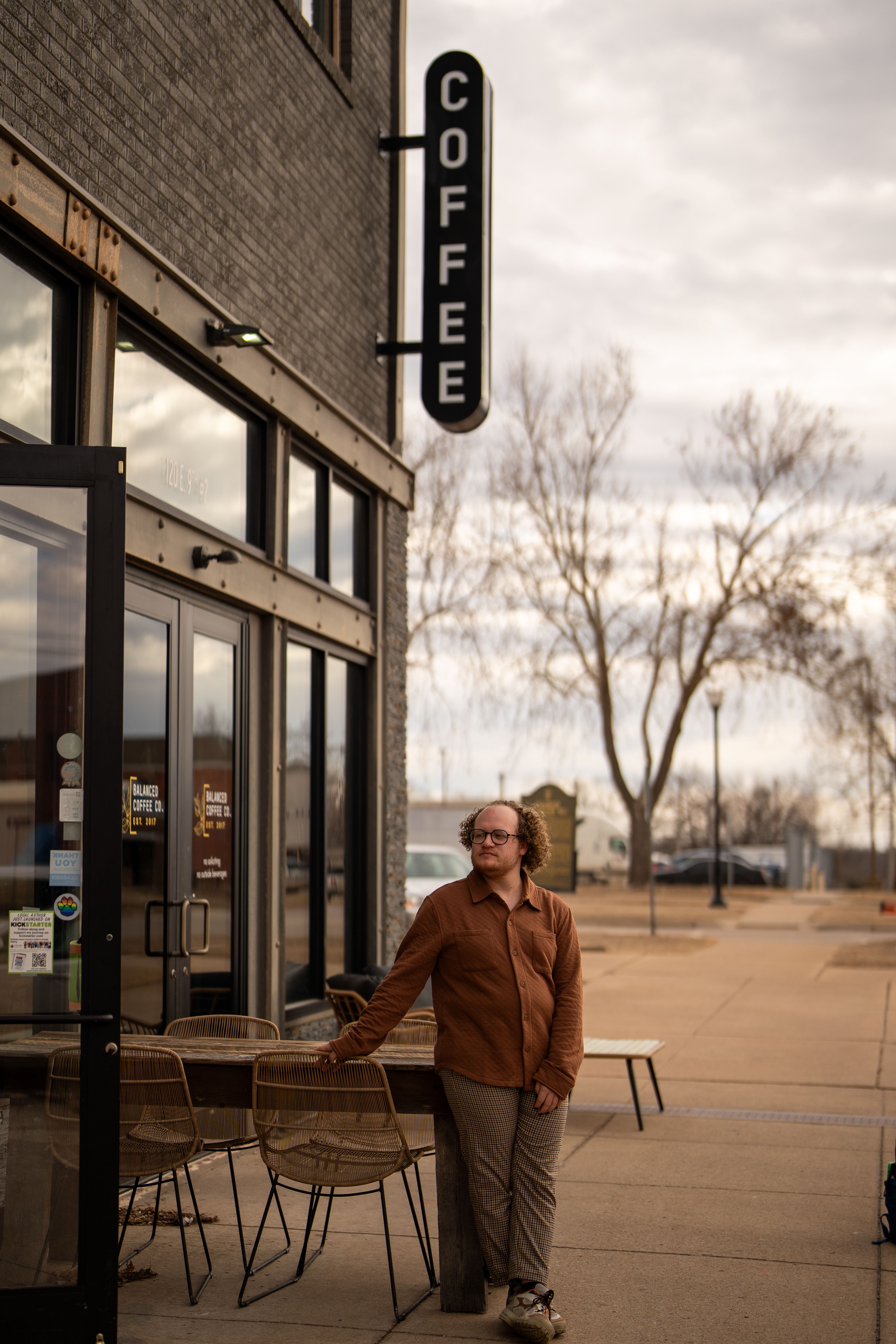 Man with curly hair stands outside a coffee shop on a cloudy day in Stillwater, Oklahoma.