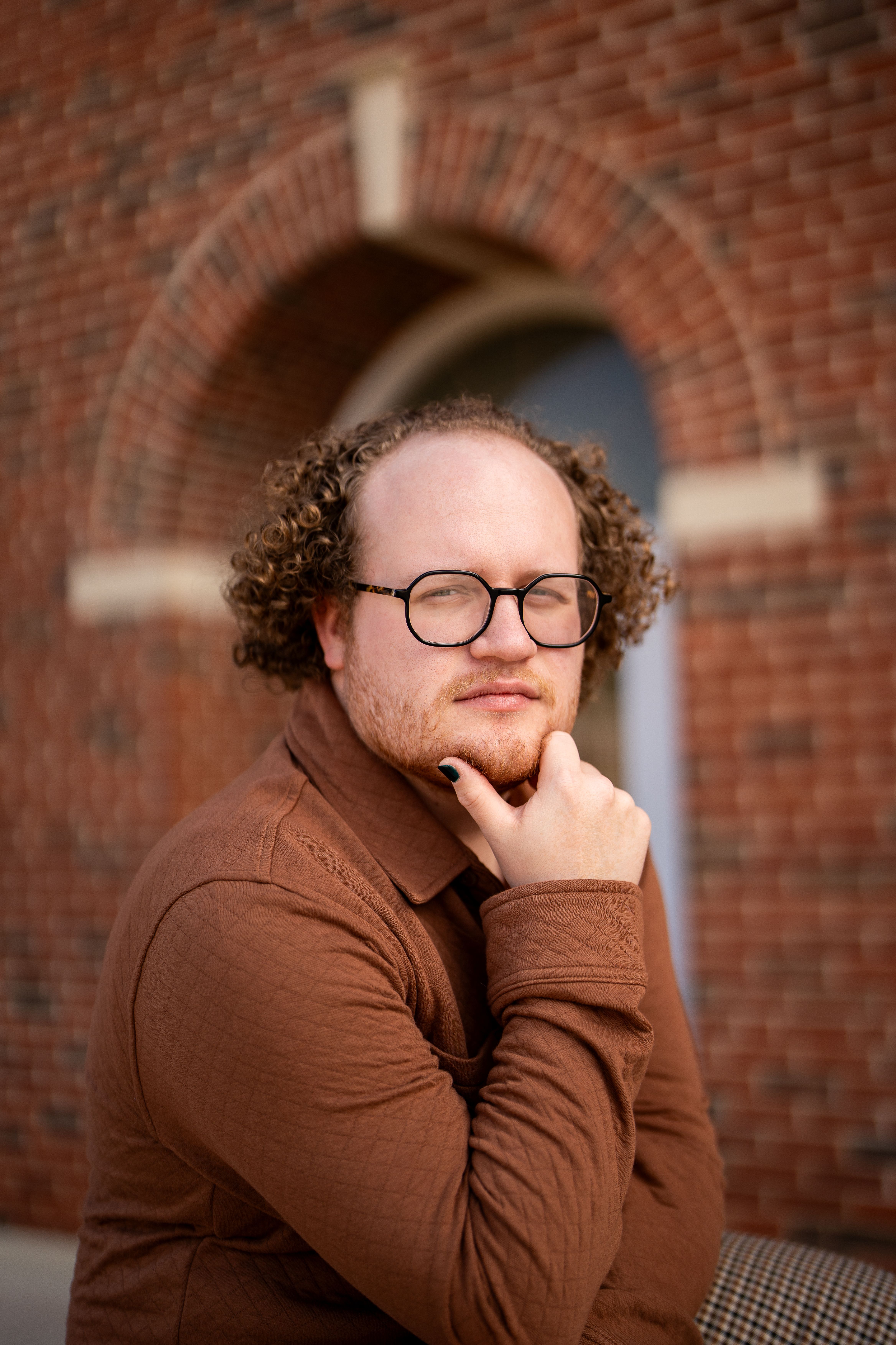 A thoughtful man poses beside a brick archway, capturing a modern, warm vibe.