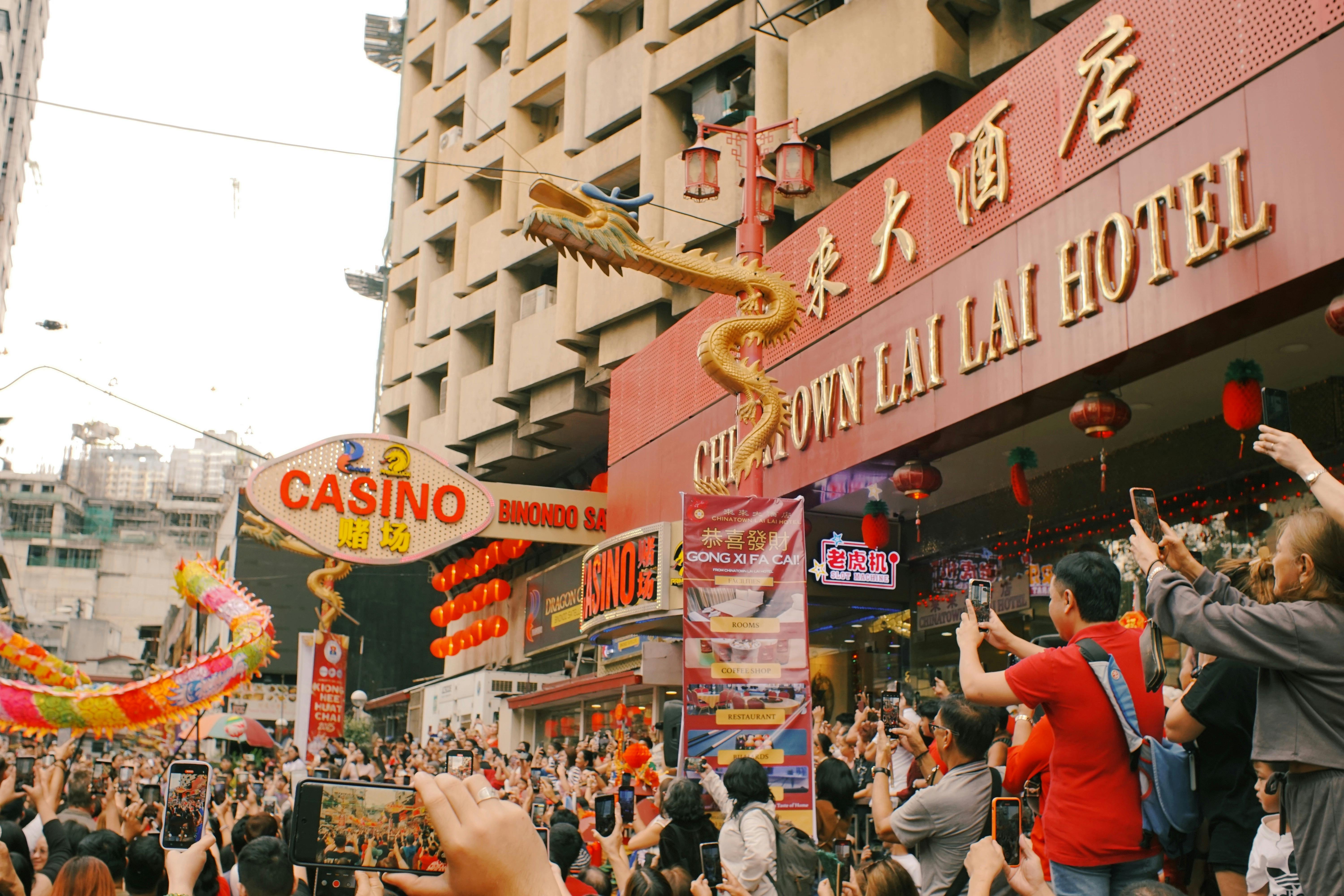 Dragon dance during a festive parade in Manila's Chinatown, drawing a crowd with smartphones.