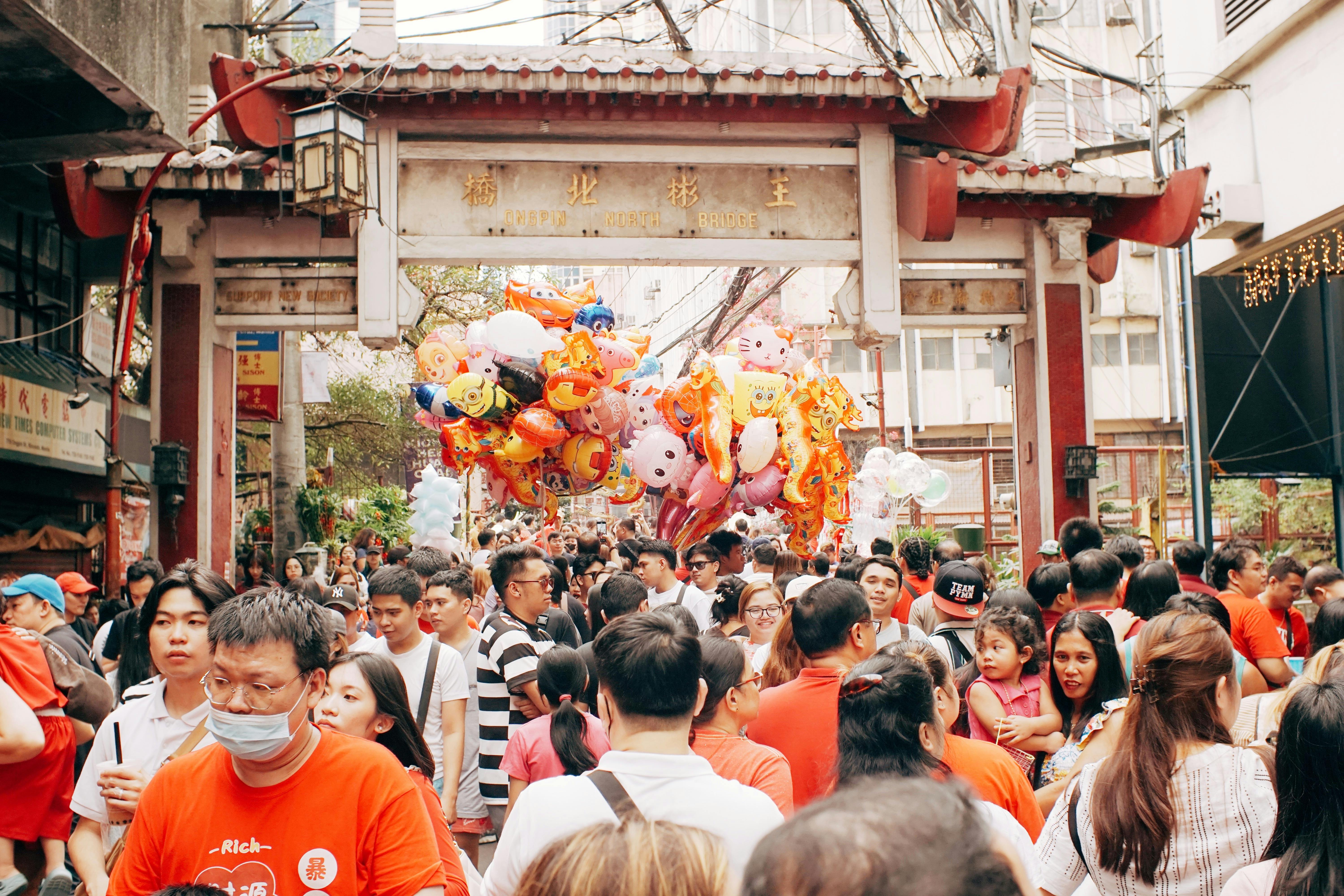 Crowded Asian market scene with colorful balloons and people celebrating outdoors.