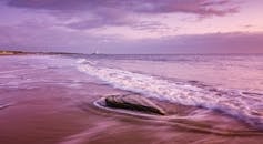 日出时分，宁静的海滩景色中，海浪与远处的灯塔共同捕捉了这份静谧之美