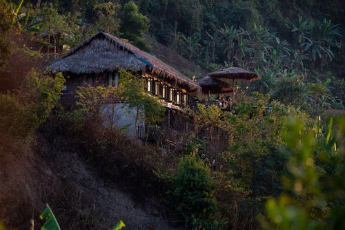 Free A traditional hut with a thatched roof nestled on a lush hillside overlooking dense jungle foliage. Stock Photo