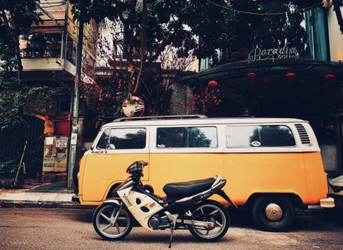 A classic orange van parked beside a modern motorcycle on a city street, showcasing urban retro vibes.