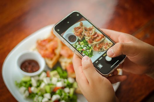 Close-up of hands photographing a brunch plate with bacon, salad, and sauce using a smartphone.