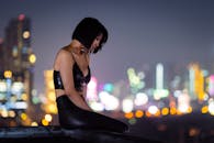 一位时尚女子身着黑色皮革，在屋顶上摆出姿势，背景的城市灯光营造出戏剧性的夜生活场景