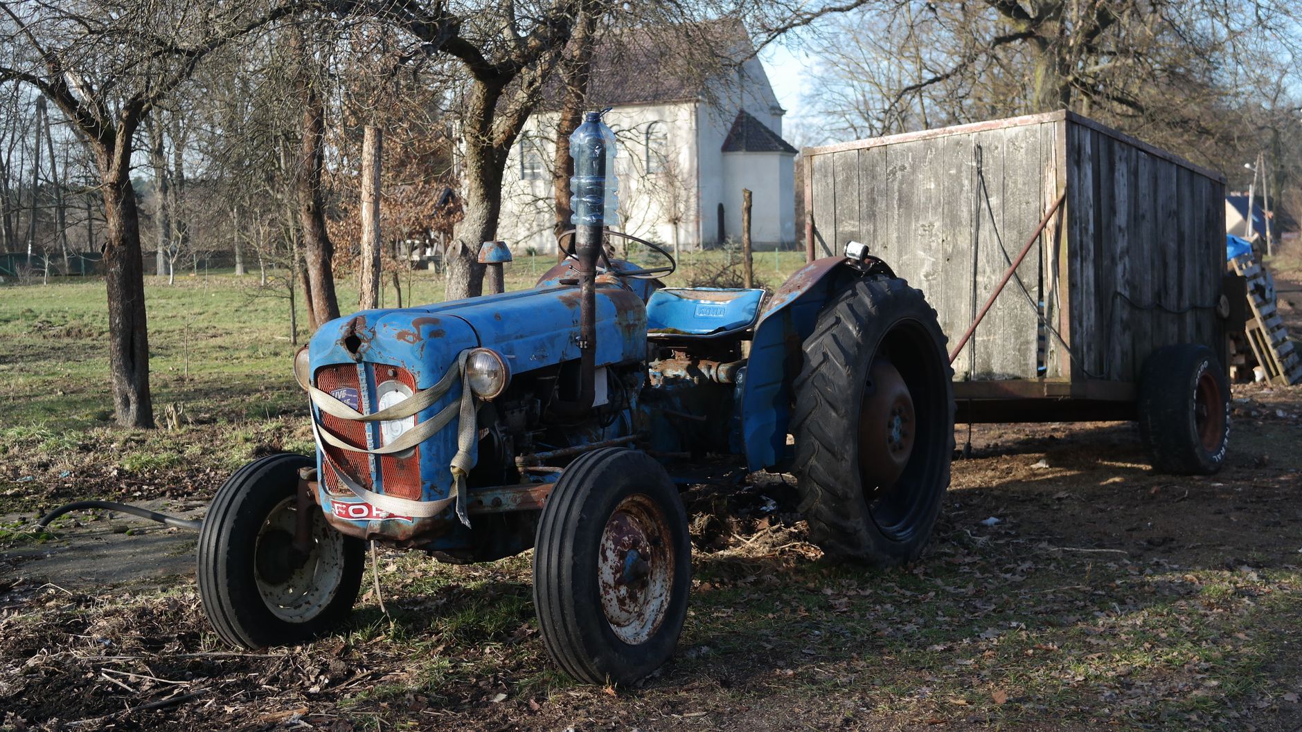 Old blue tractor in rustic setting with cart, capturing rural life's simplicity.