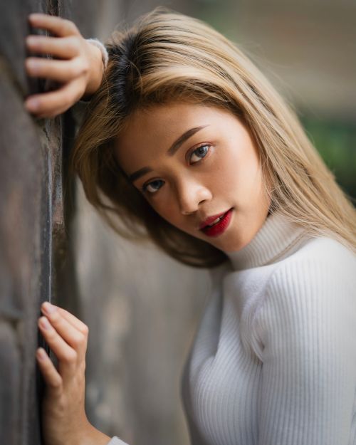 Free Stylish portrait of a young woman leaning against a stone wall in a natural outdoor setting. Stock Photo