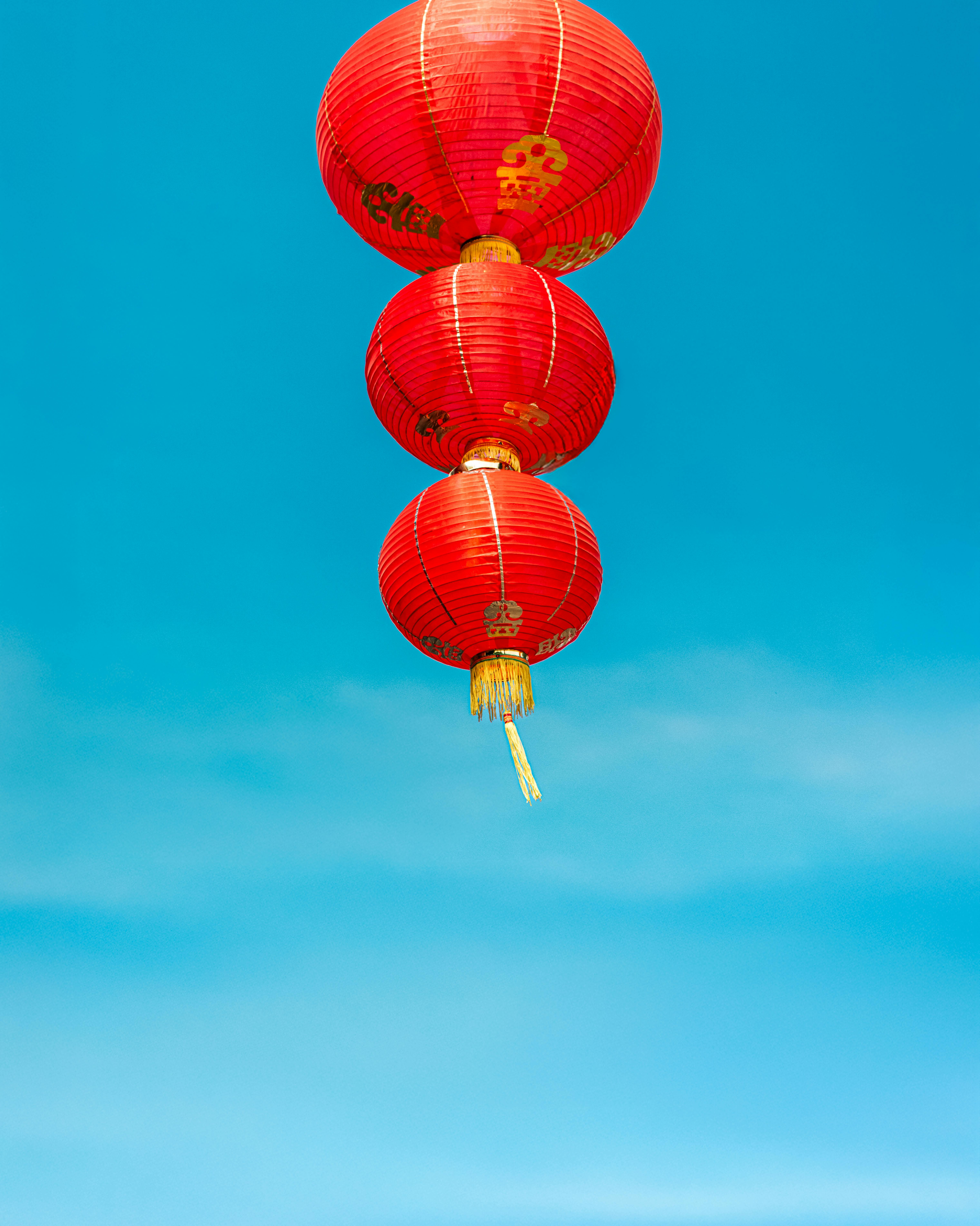 Red Chinese lanterns floating against a clear blue sky, symbolizing celebration and festivity.