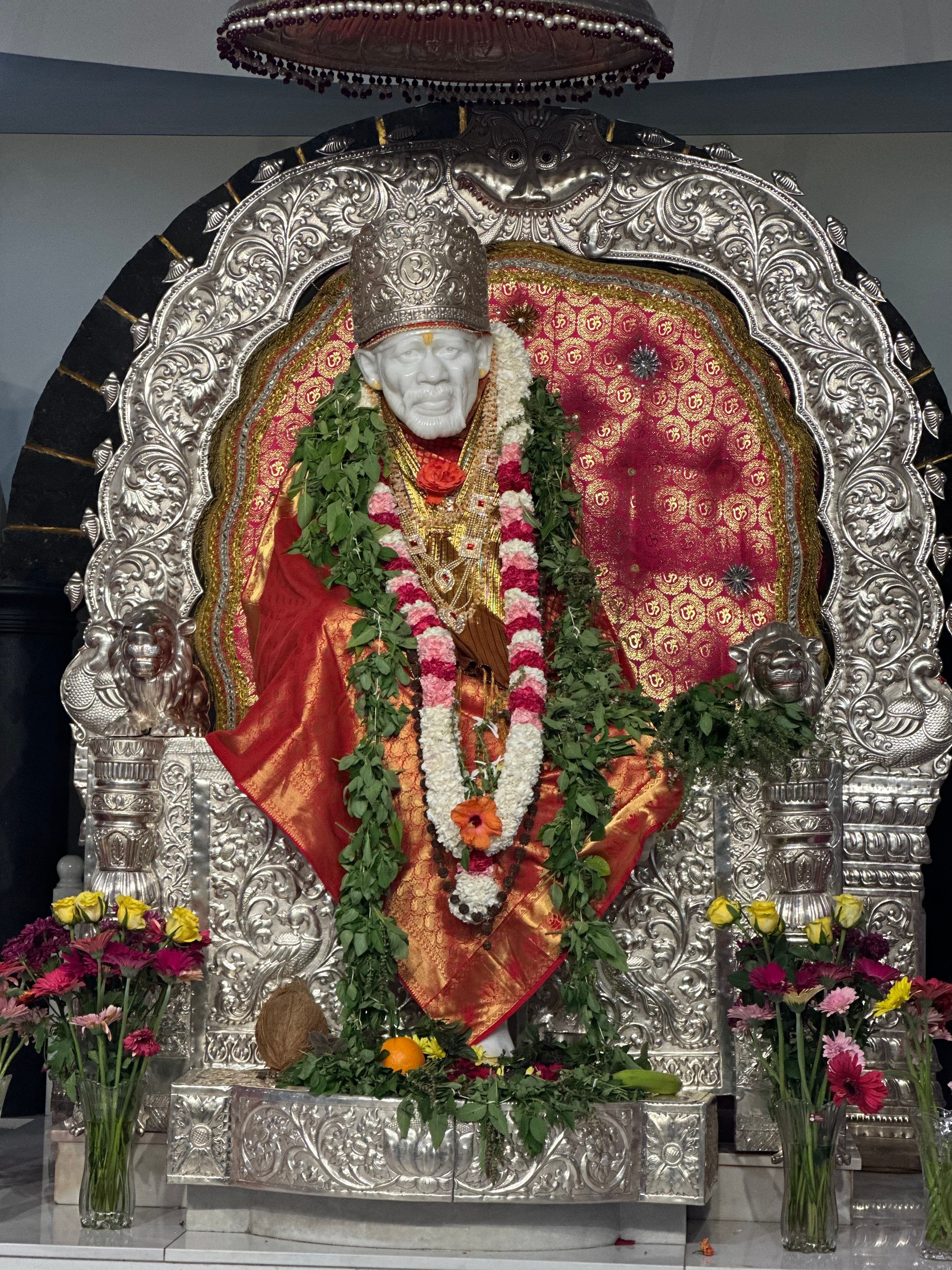 A detailed depiction of a Saibaba statue draped with vibrant flower garlands in a temple setting.