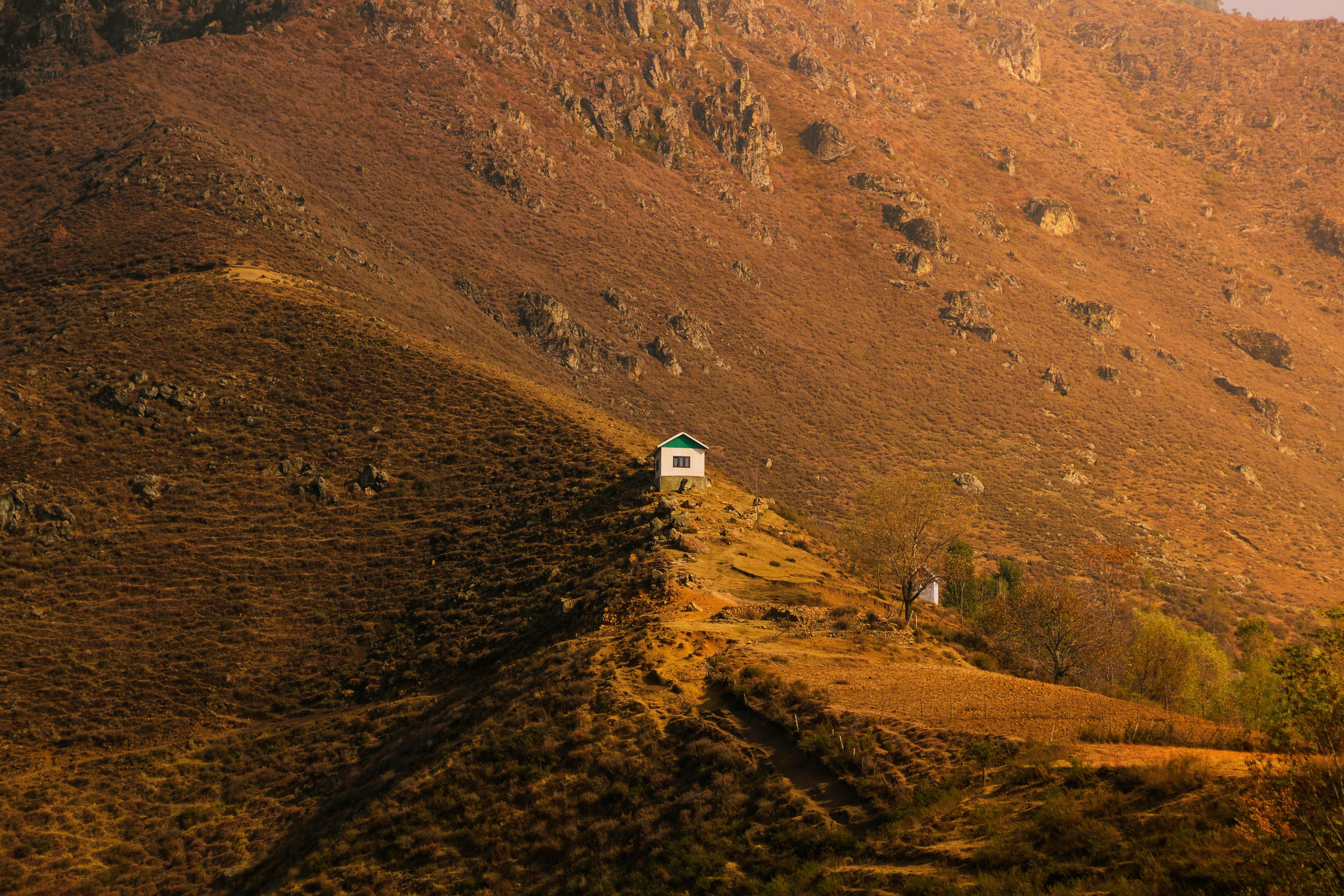 Explore a lone house nestled in a serene, rugged mountain landscape bathed in warm light.