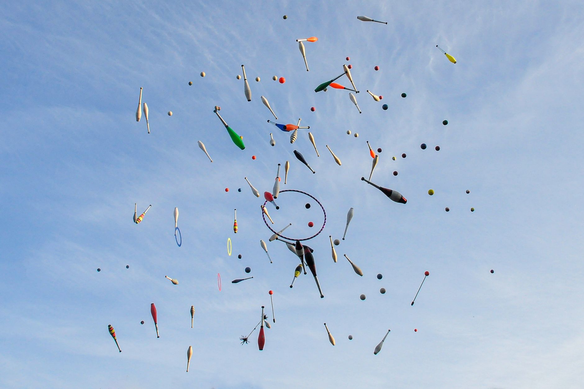 Vibrant juggling props in mid-air against a bright blue sky, showcasing motion and creativity.