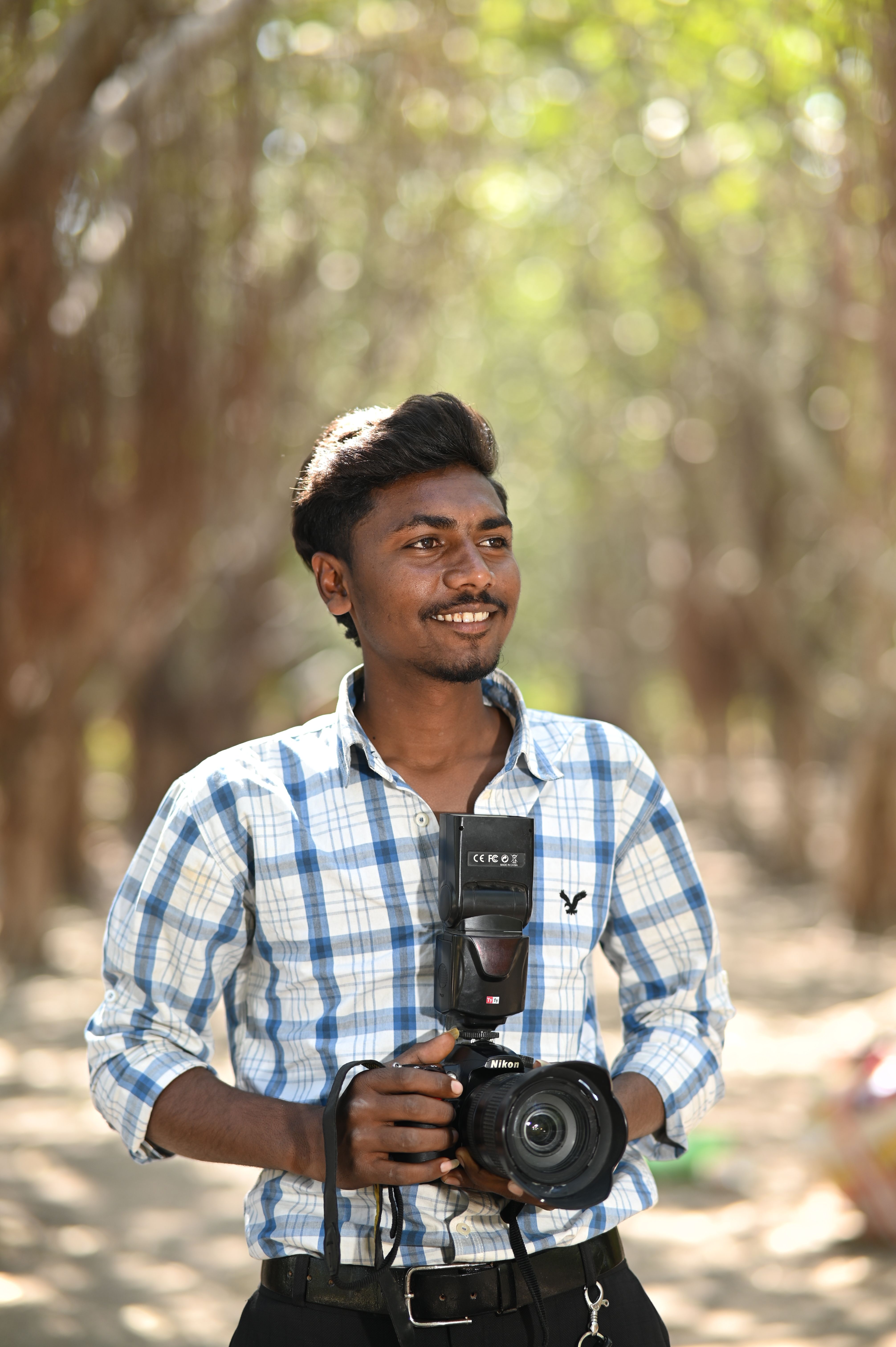 A joyful photographer holding a camera in a sunlit forest setting.