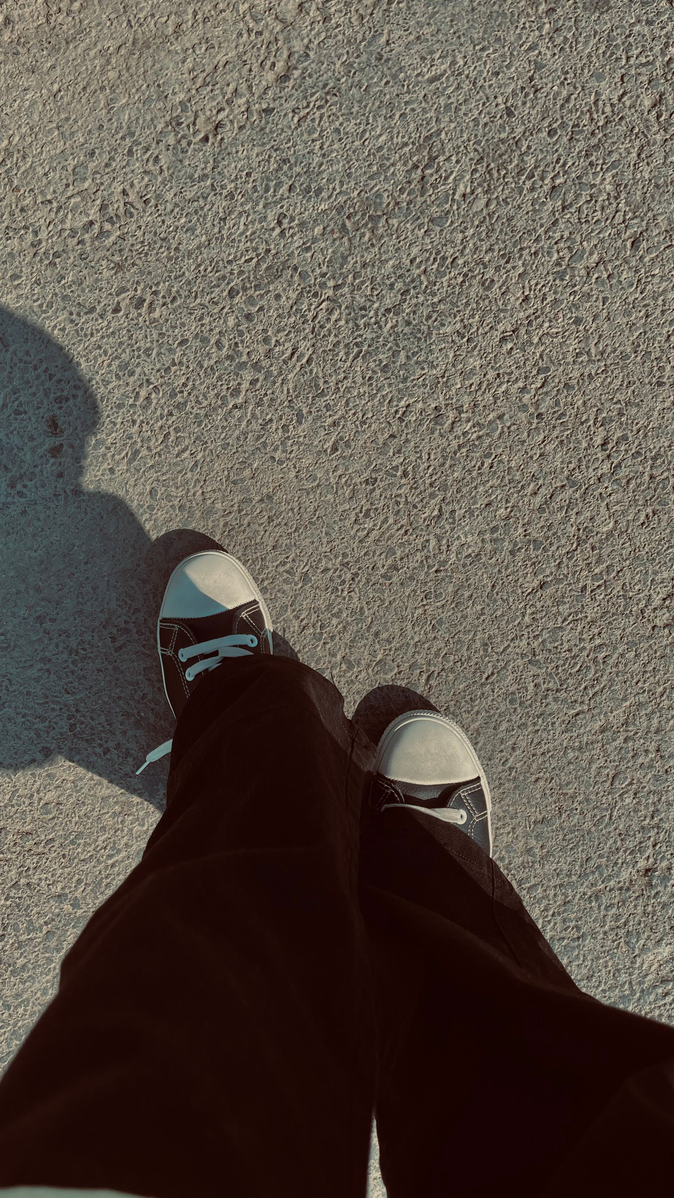 Top-down view of sneakers worn on a concrete path, casting a shadow.