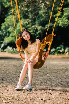 一个年轻女子穿着休闲服装，在阳光明媚的公园里，享受着秋千上的宁静时刻