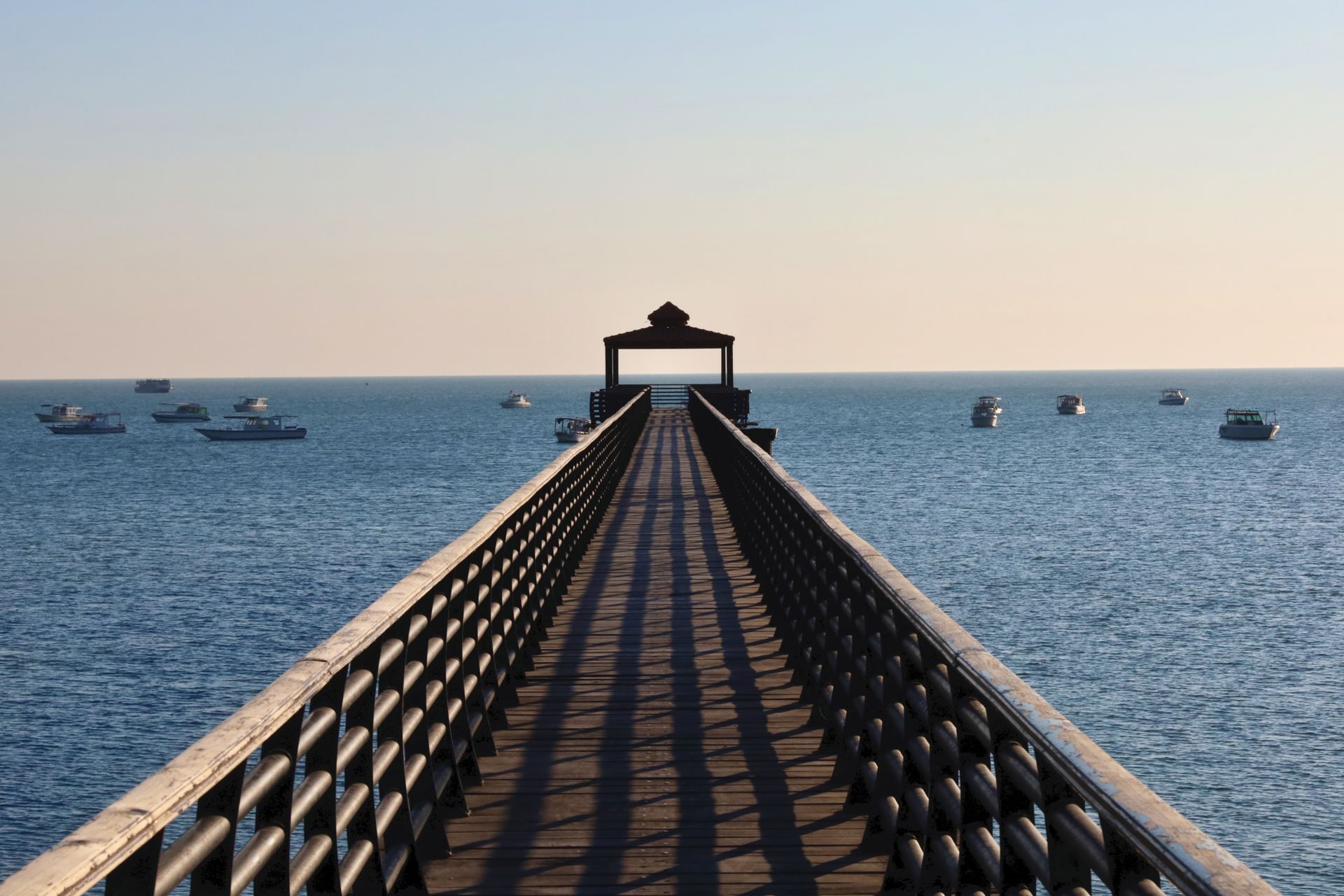 Peaceful scene of a wooden pier over the ocean with boats in a calm, clear day.