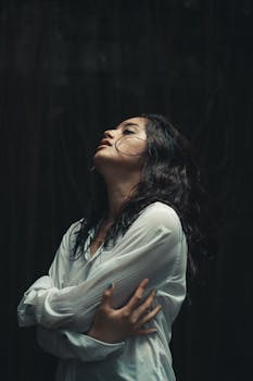 一名女子身穿白色衬衫，在黑暗背景下若有所思地摆出姿势