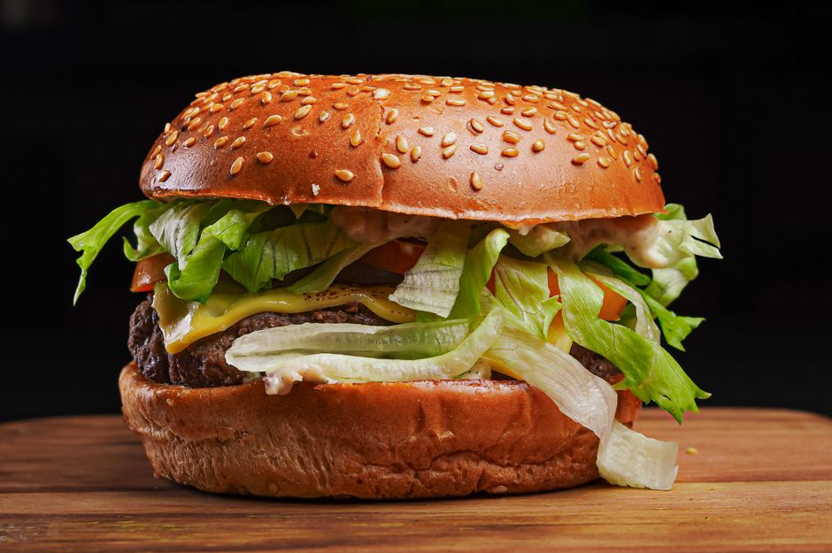 Close-up of a juicy cheeseburger with fresh lettuce and sesame seed bun on a wooden board.