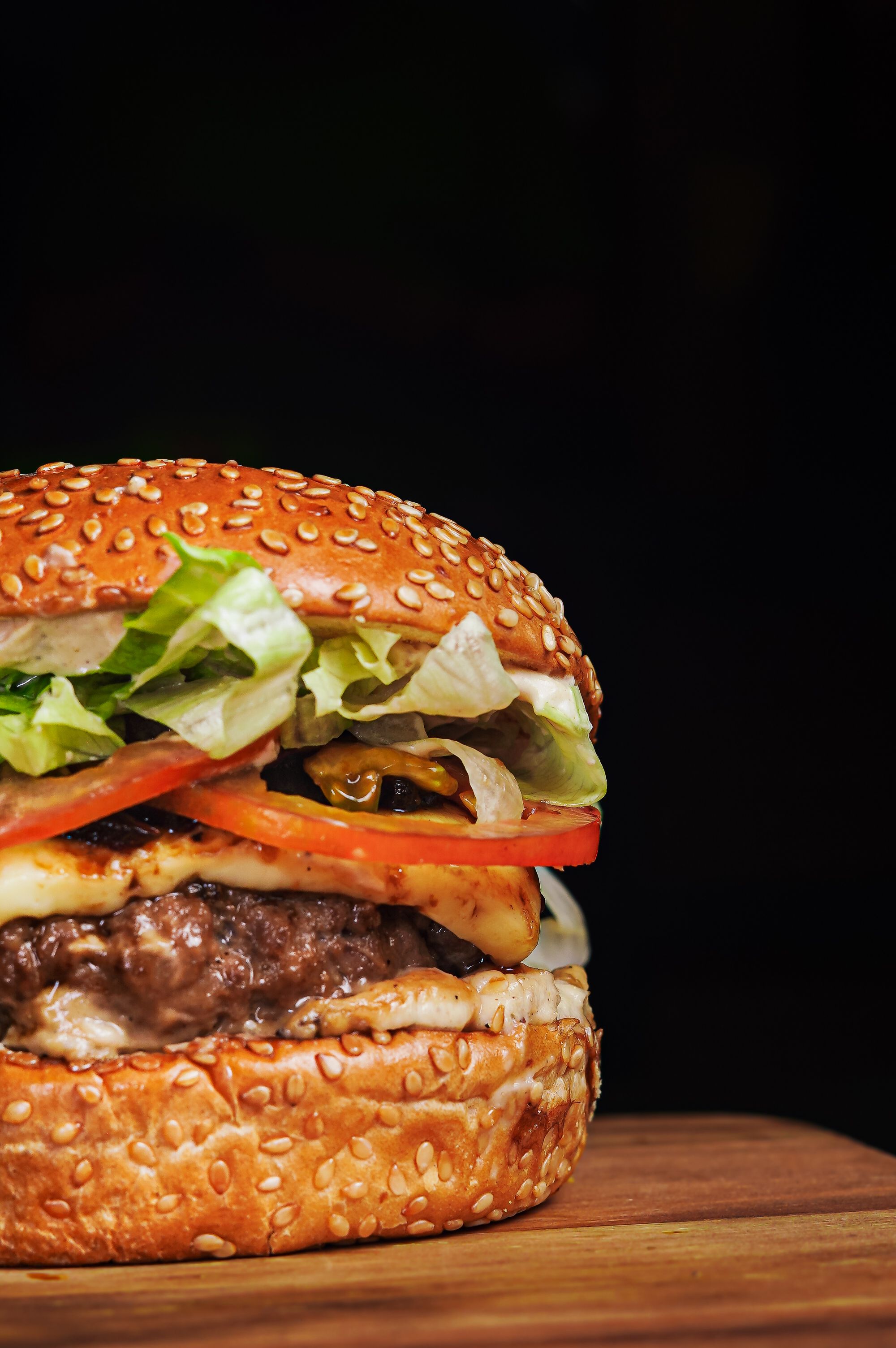 Close-up of a juicy gourmet cheeseburger with lettuce, tomato, and cheese on a wooden board.