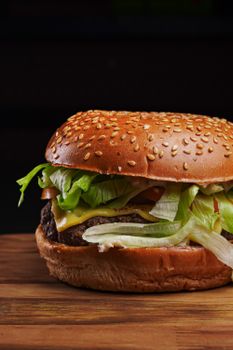 Juicy cheeseburger with fresh lettuce, tomato, and a sesame seed bun on a wooden table.