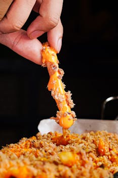Close-up of a hand lifting cheesy finger food with toppings.