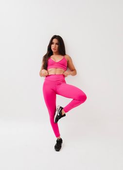 Athletic woman in pink workout attire posing in a studio setting, demonstrating fitness and style.