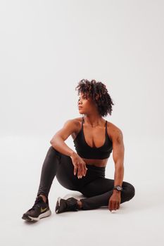 Young athletic woman in black activewear sitting on the floor against a white background.