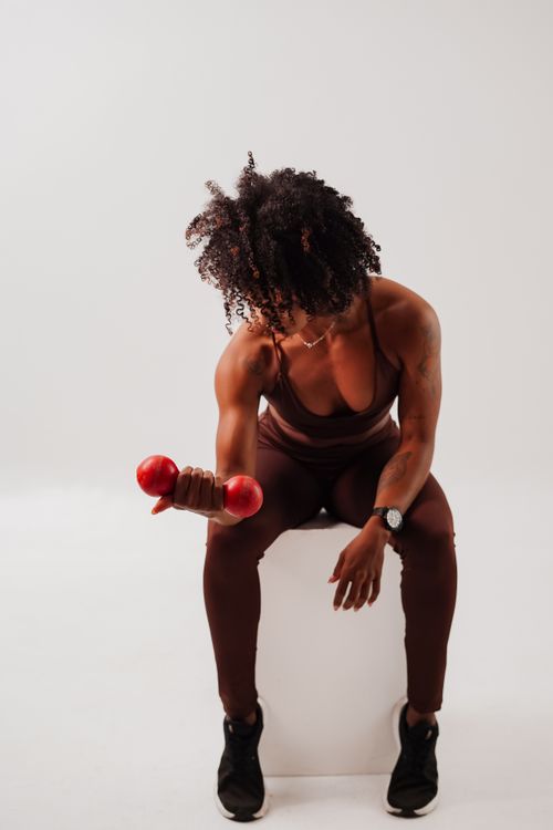 Free Athletic woman in a seated curl with red dumbbell, promoting strength and fitness. Stock Photo