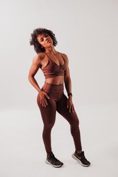 Confident woman standing in brown activewear, posed against a minimalist white background.