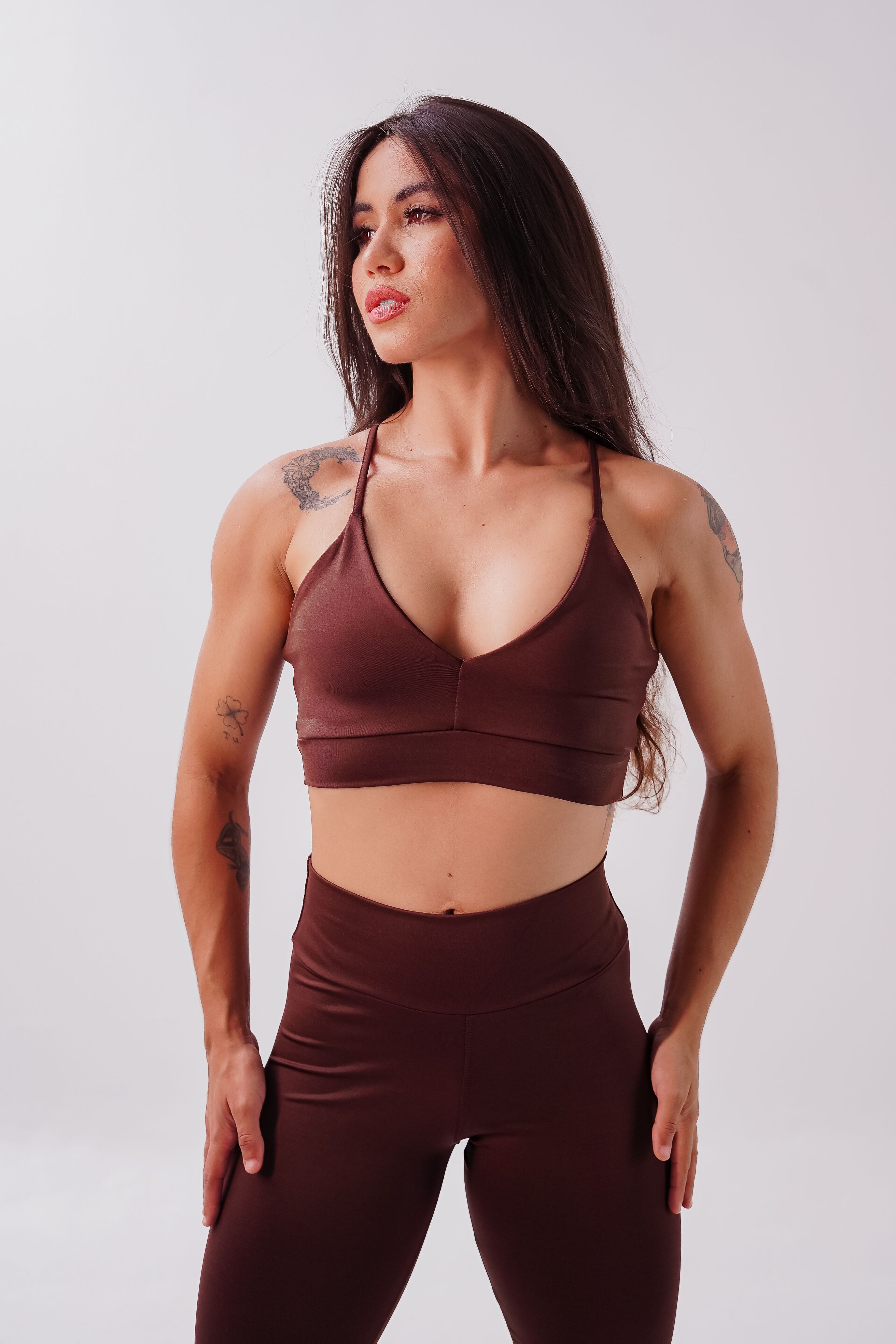 Mulher atlética em um traje de exercício marrom posando confiantemente contra um fundo neutro.