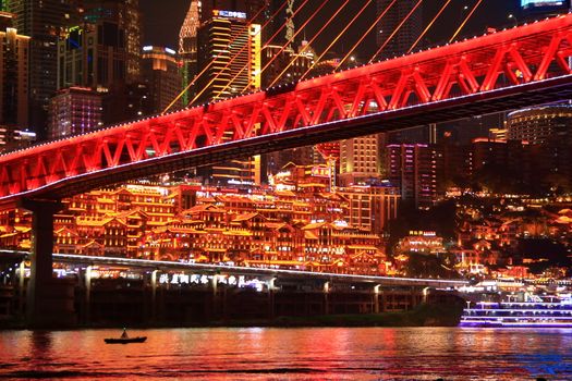 Vibrant night view of Chongqing with illuminated buildings and a striking red bridge.