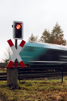 Blurred high-speed train passing a railway crossing with a red signal in a forested area.