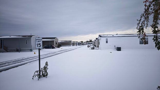 A serene winter scene with snow-covered mobile homes and a speed limit sign.