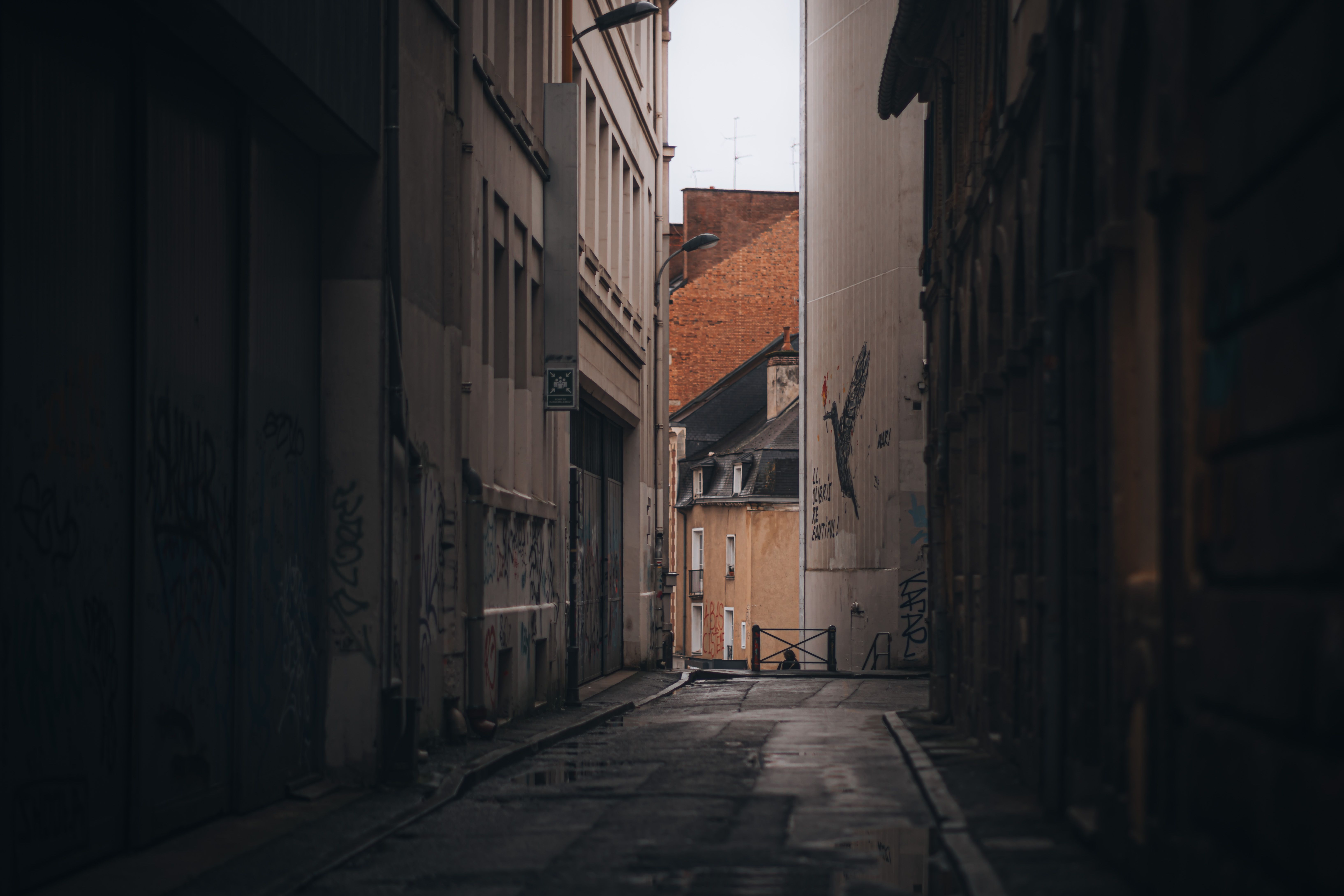 Une scène de ruelle de mauvaise humeur entre des bâtiments avec des graffitis urbains et un éclairage tamisé.