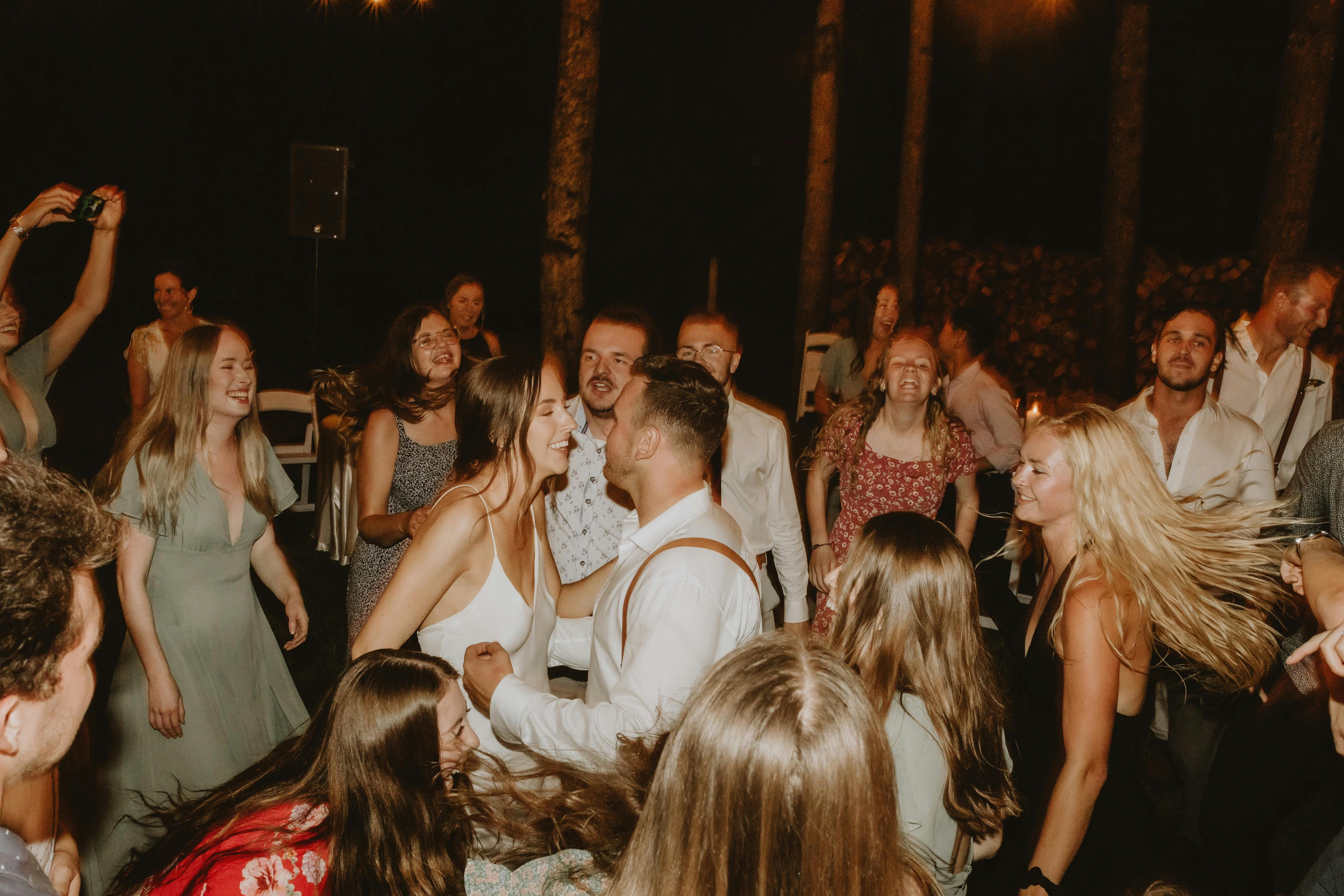 A vibrant night dance scene at an outdoor wedding reception with lively guests.