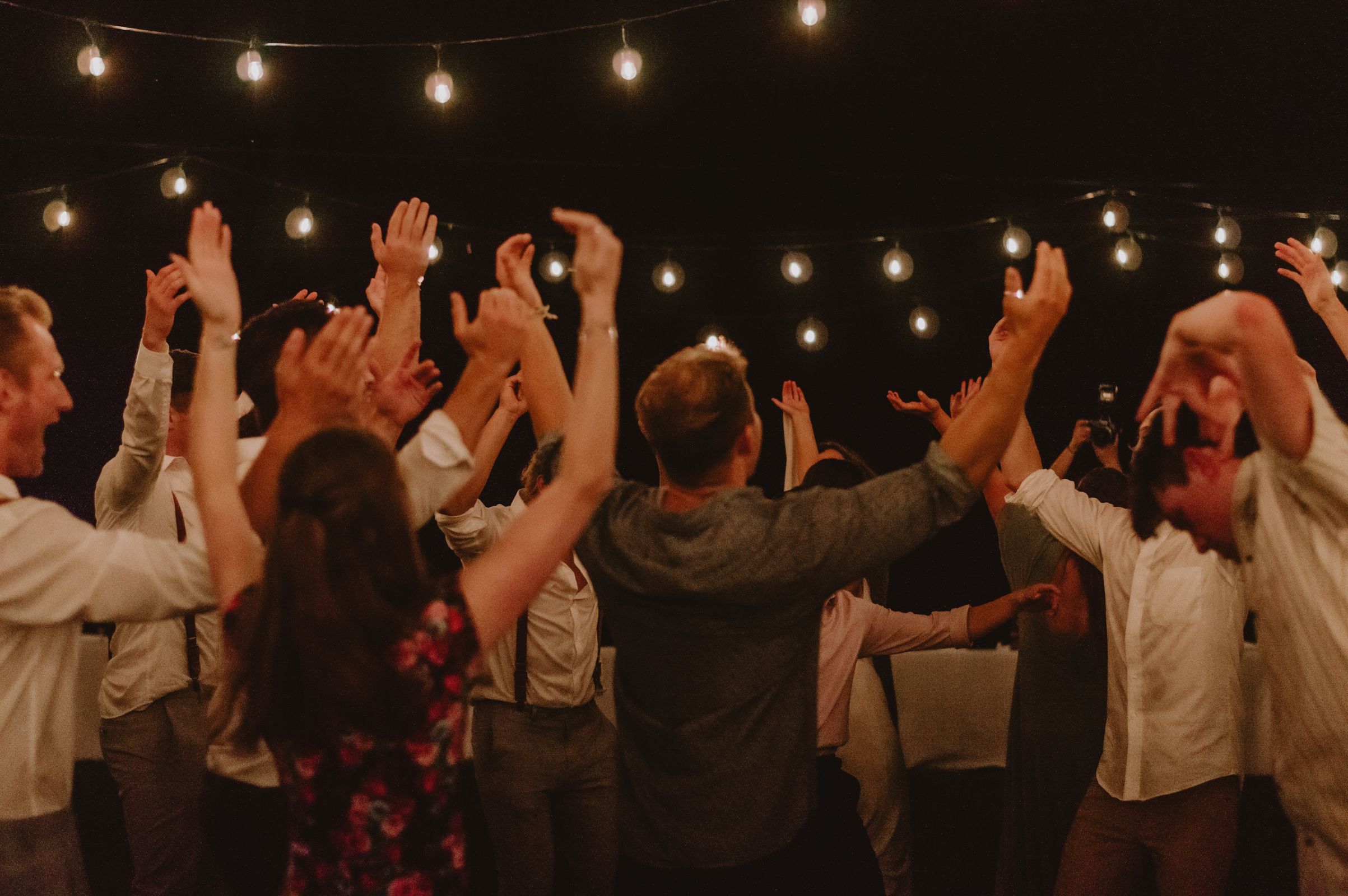 Group of adults dancing energetically under string lights at night