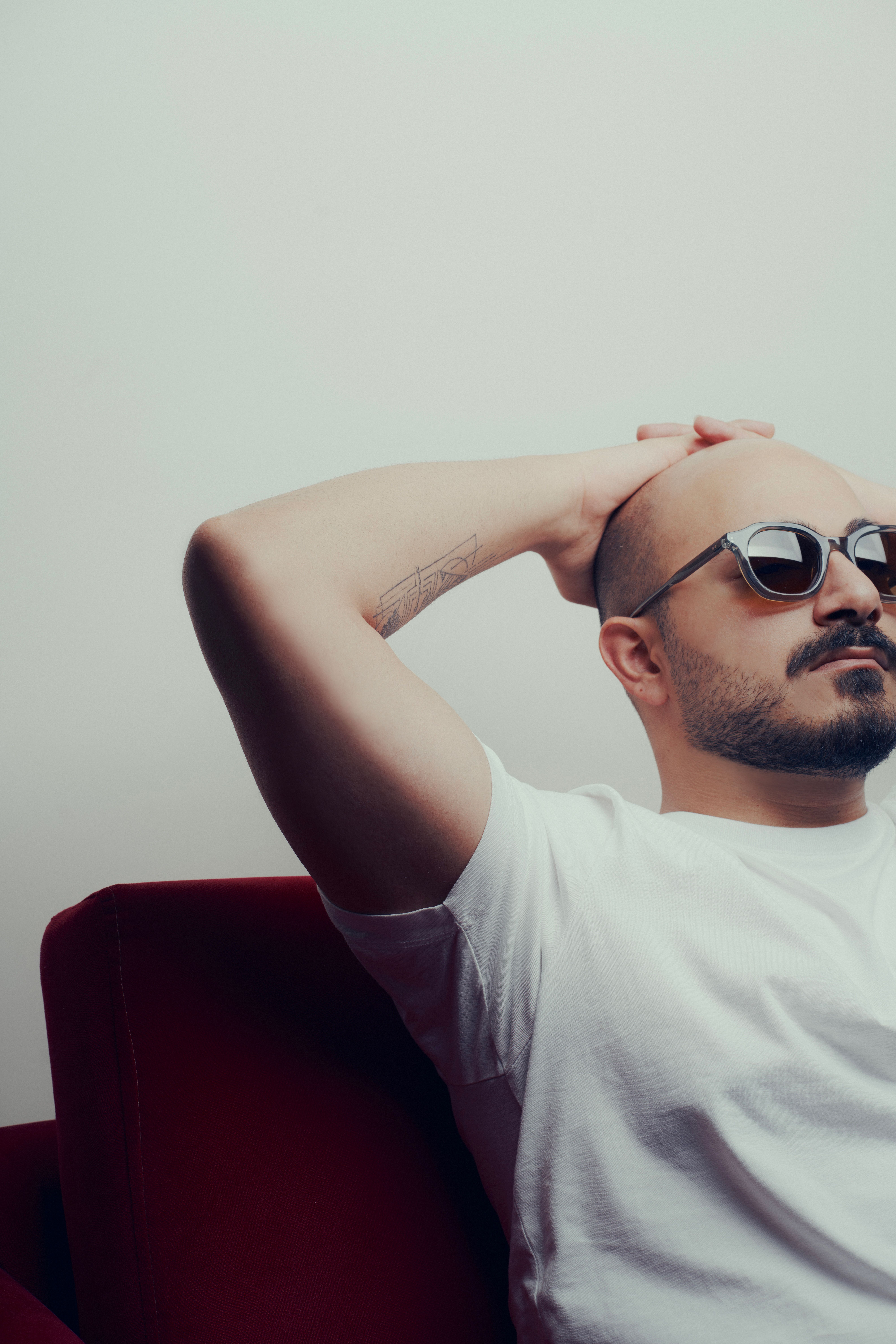 Casual portrait of a relaxed man in sunglasses sitting on a red armchair indoors.