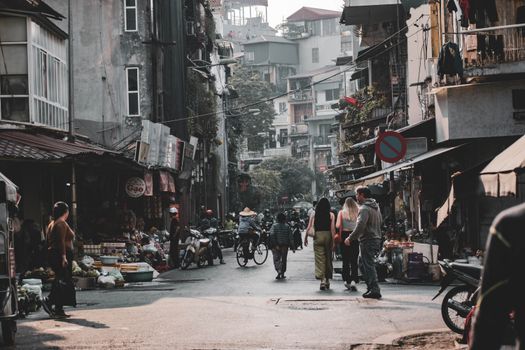 Bustling Hanoi street with people, shops, and motorbikes on a lively day.