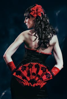 A woman in an elegant black dress with a red fan poses against a dark background.