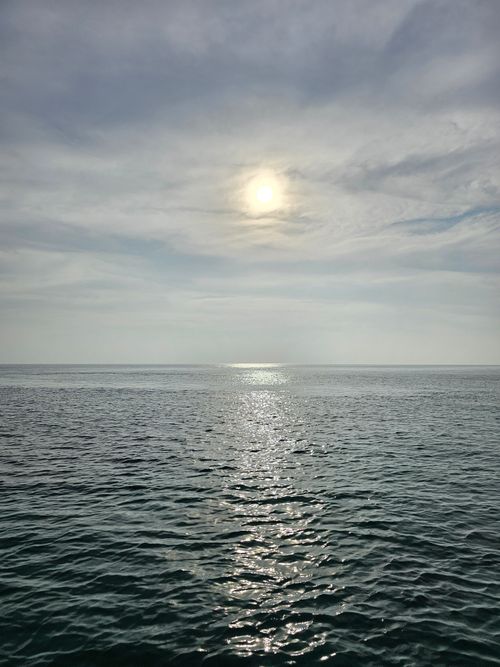 Free Calm ocean waters reflecting sunlight under a cloudy sky, creating a serene scene. Stock Photo