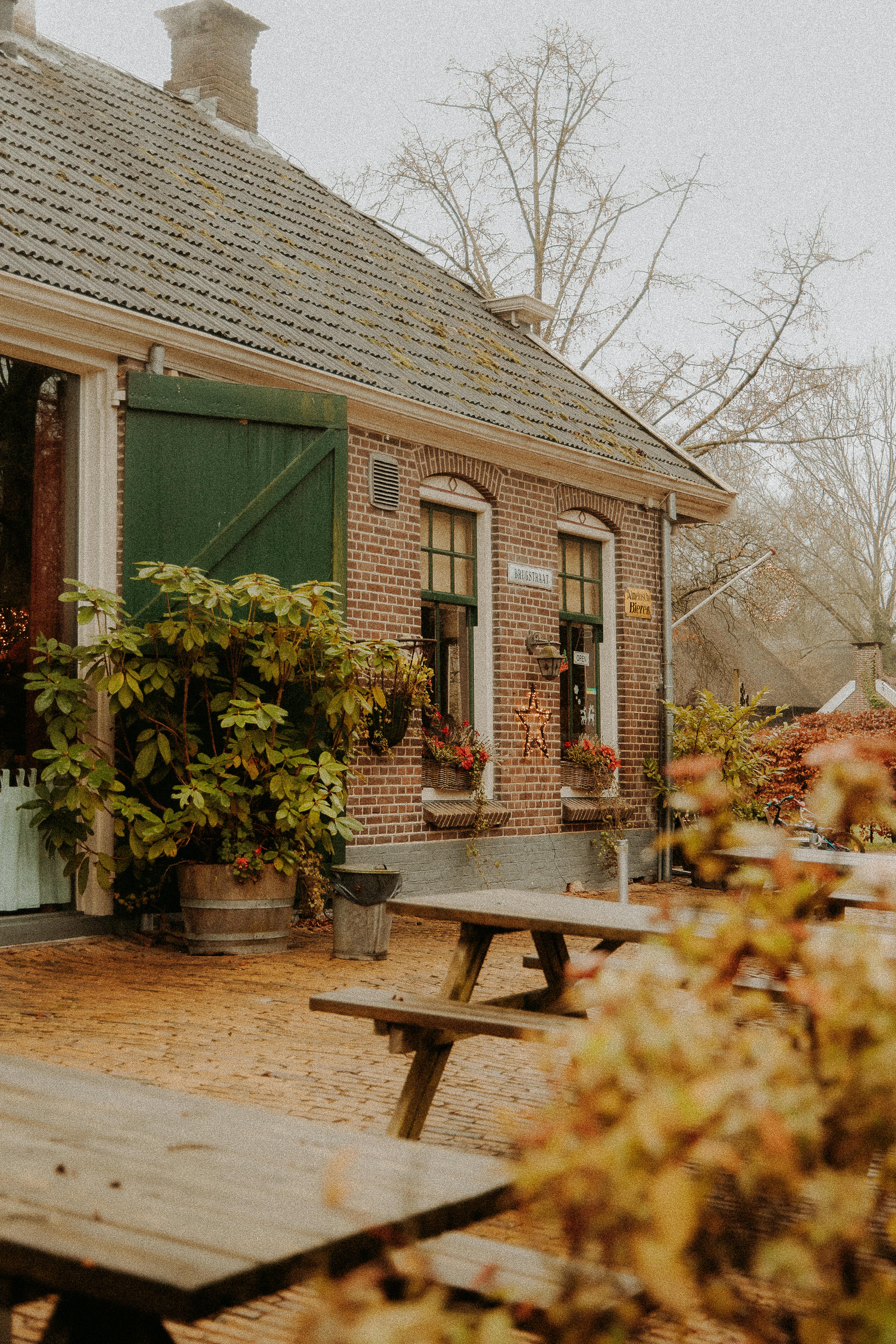 Brick house with green shutters and autumn foliage, reflecting rustic village charm.
