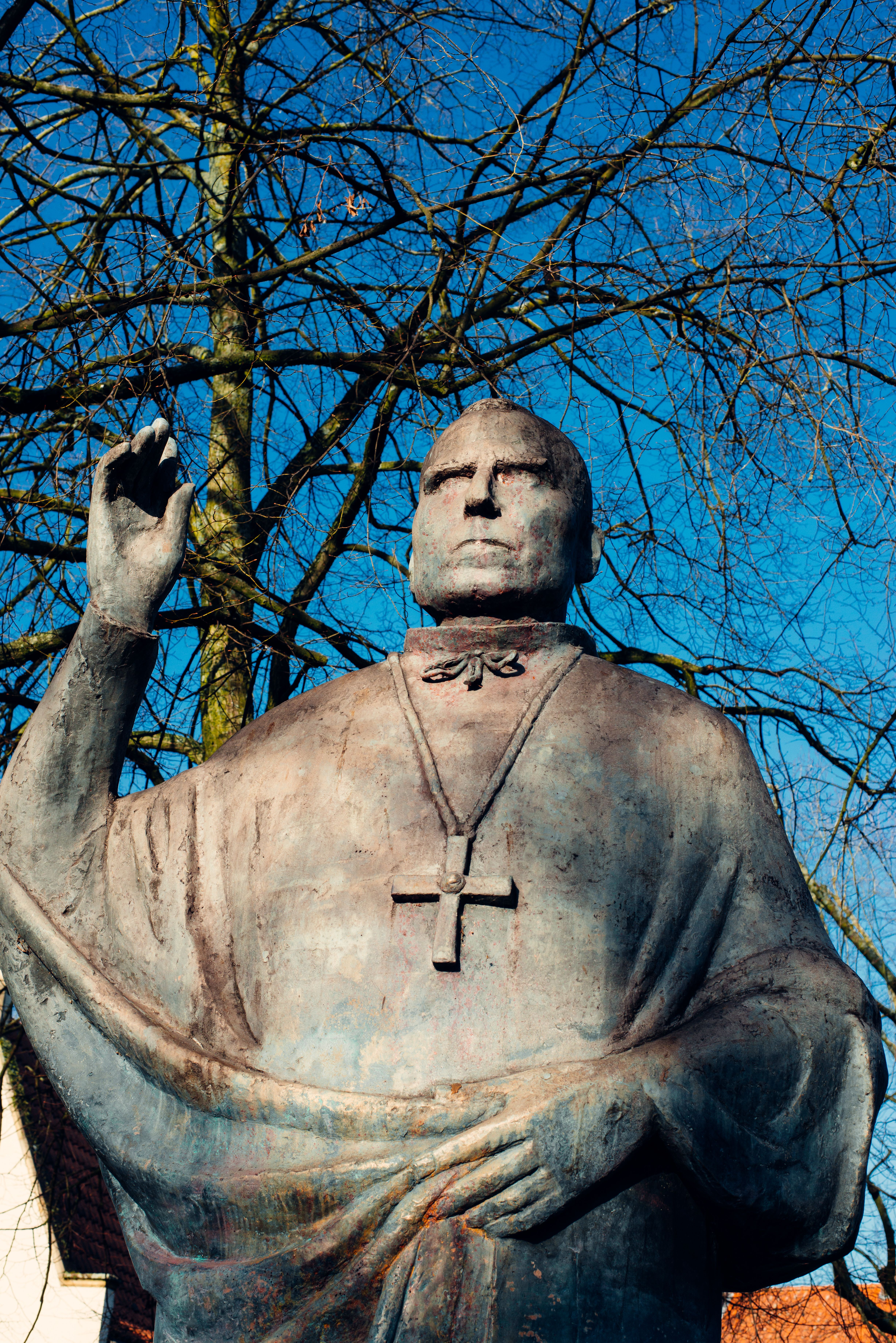 Bronze statue of a religious figure with cross pendant under clear blue sky.