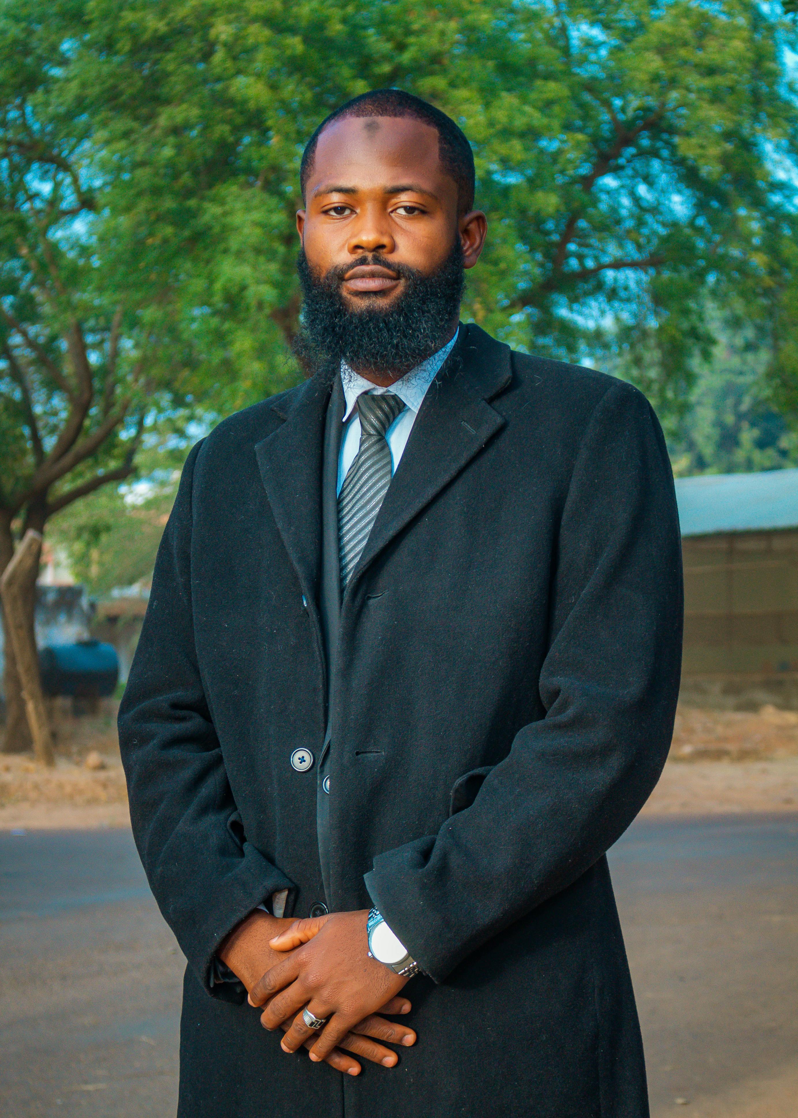 Portrait of a well-dressed man outdoors in Zaria, Nigeria, set against a natural backdrop.