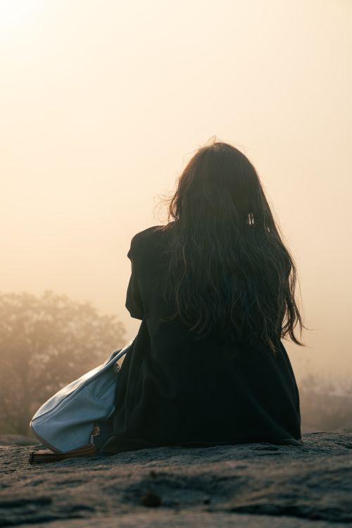 Free A woman sits outdoors on a misty day, gazing at nature with a contemplative mood. Stock Photo