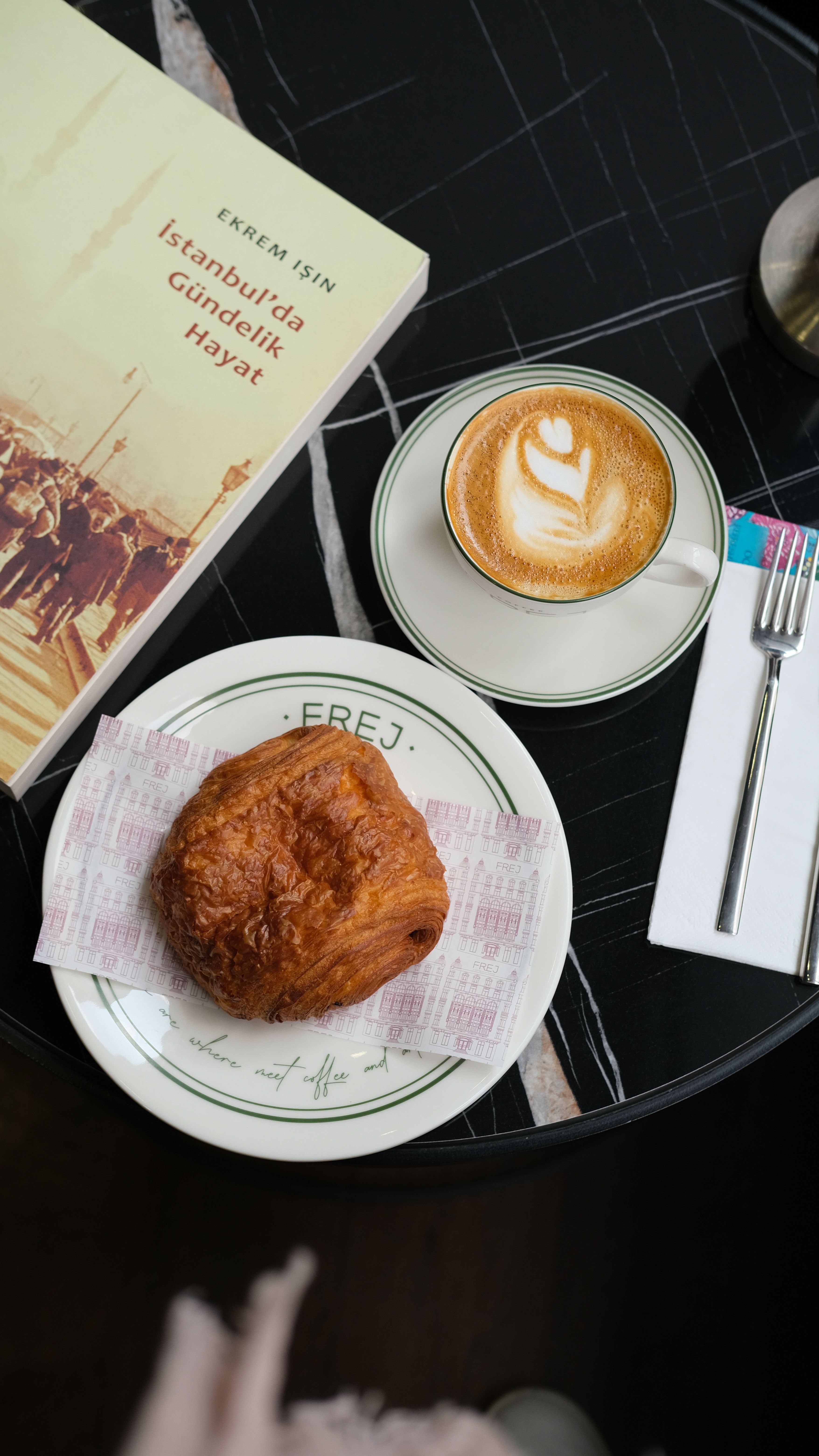 A cozy café scene with a latte, croissant, and a book on a round table.