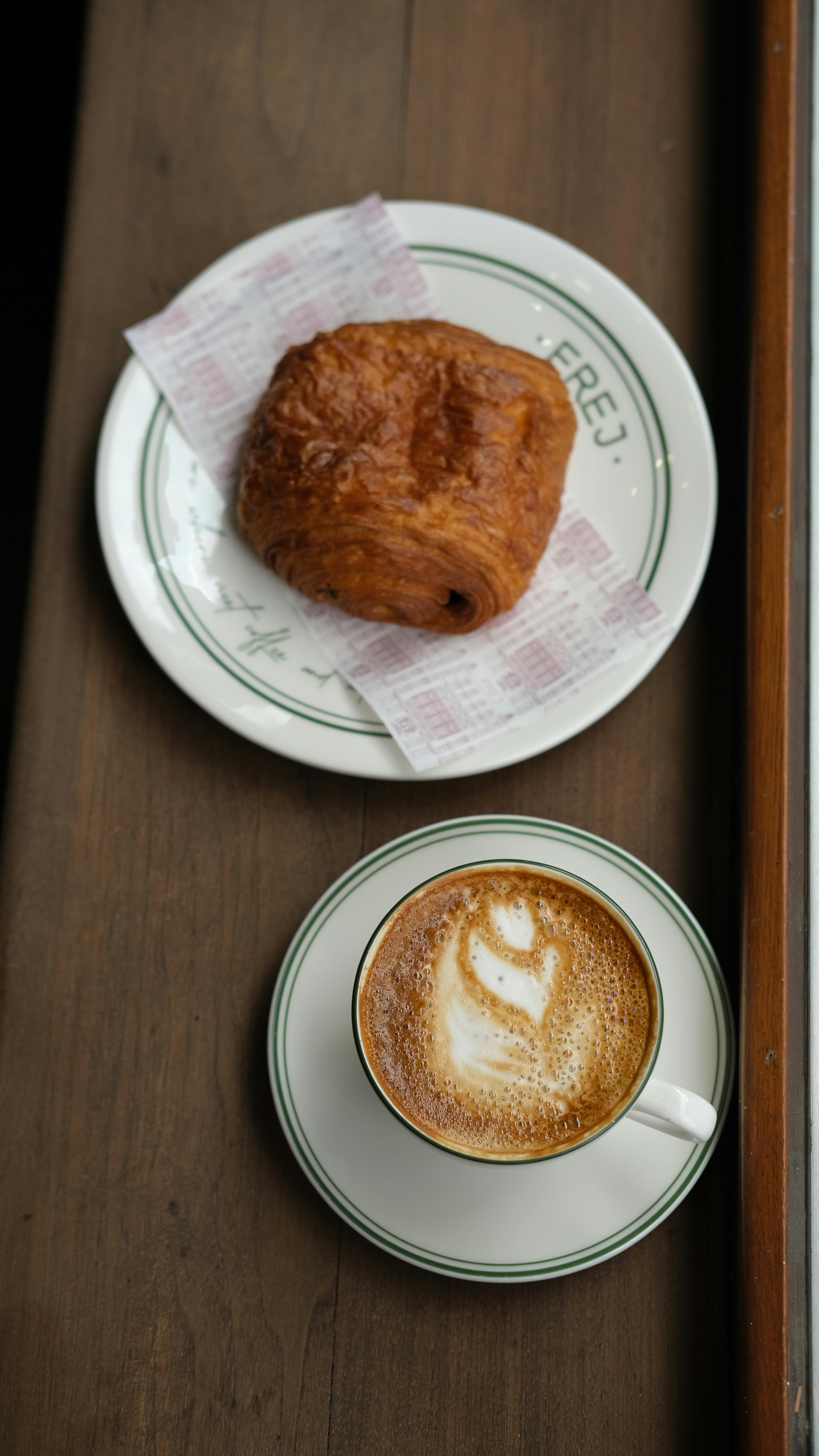 A warm cappuccino and flaky croissant on a plate, perfect for a cozy breakfast setting.