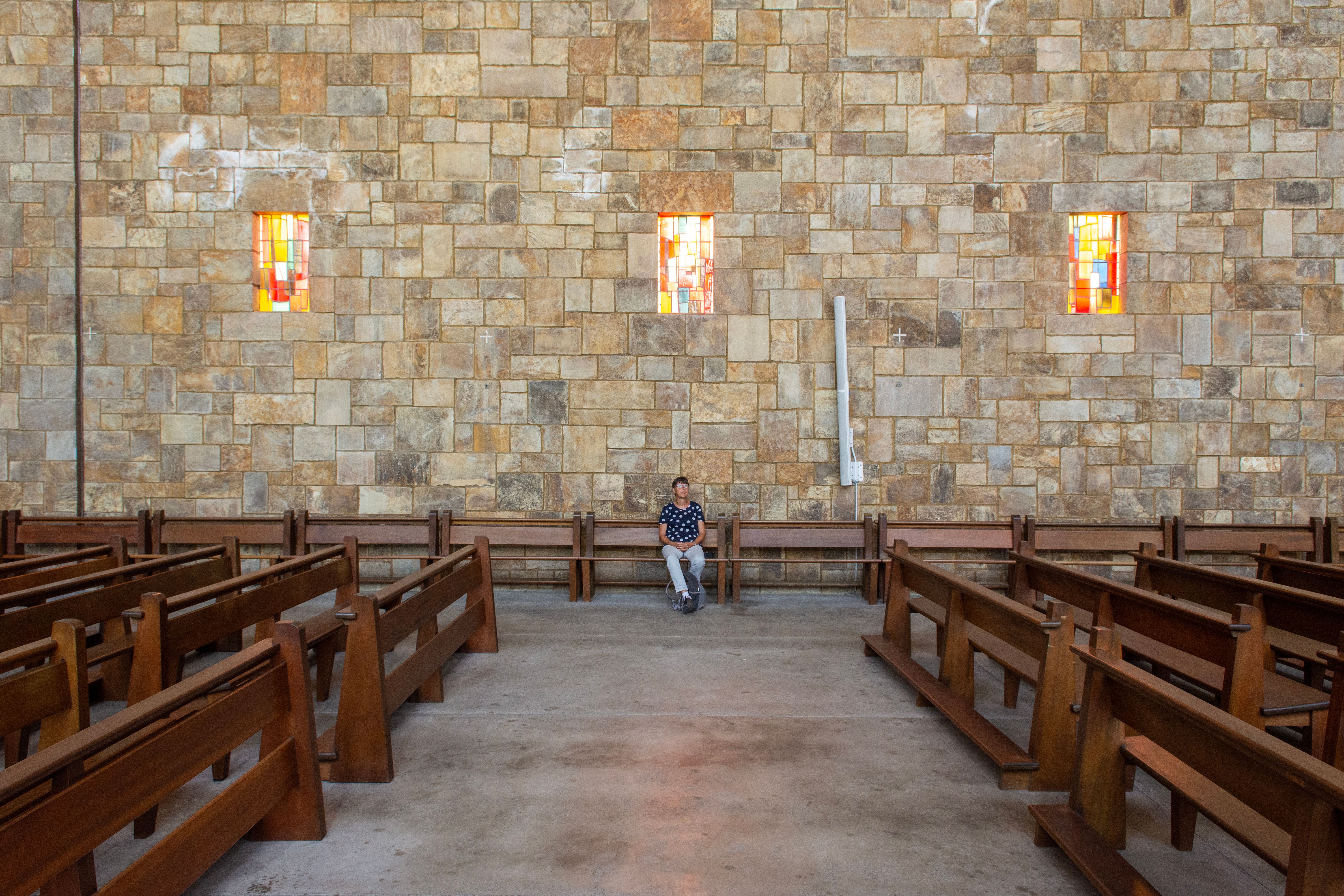 A person in meditation pose sitting in a church pew, soft light filtering through stained glass