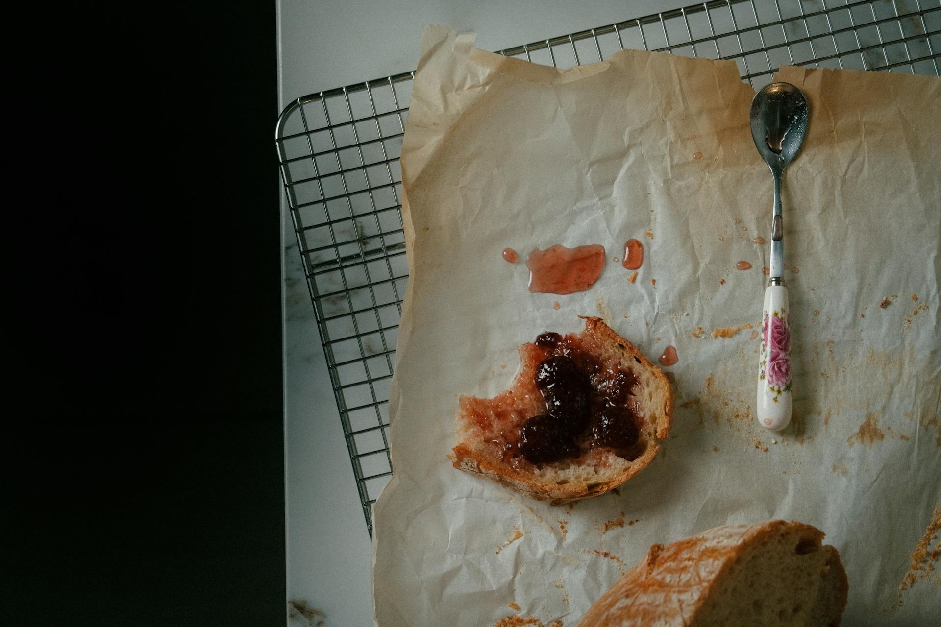 A slice of bread with jam on parchment paper and floral spoon.
