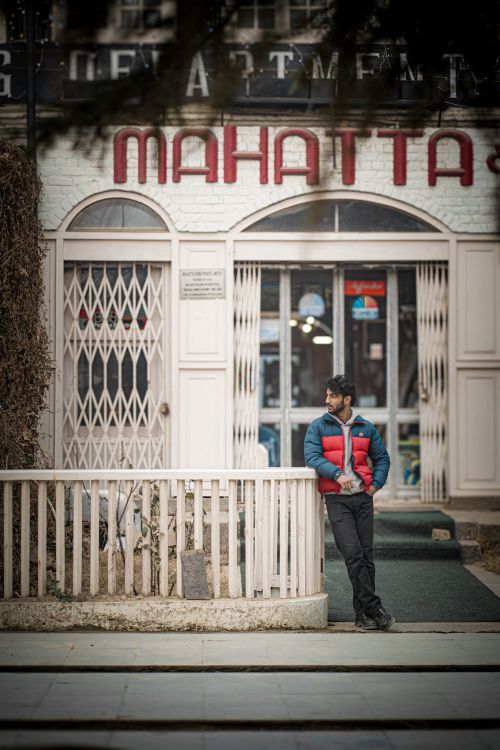 Free Man in red jacket leaning on fence outside store with Mahatta sign. Stock Photo