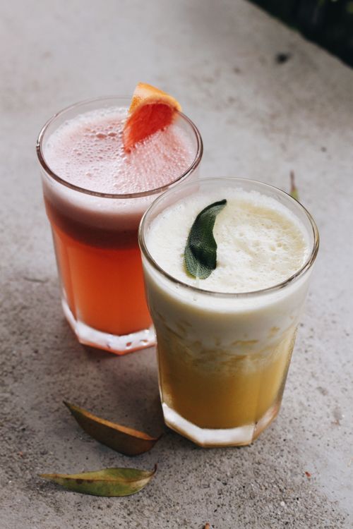Free Two vibrant citrus and tropical fruit drinks in glasses on a textured table, garnished with fruit slices and leaves. Stock Photo